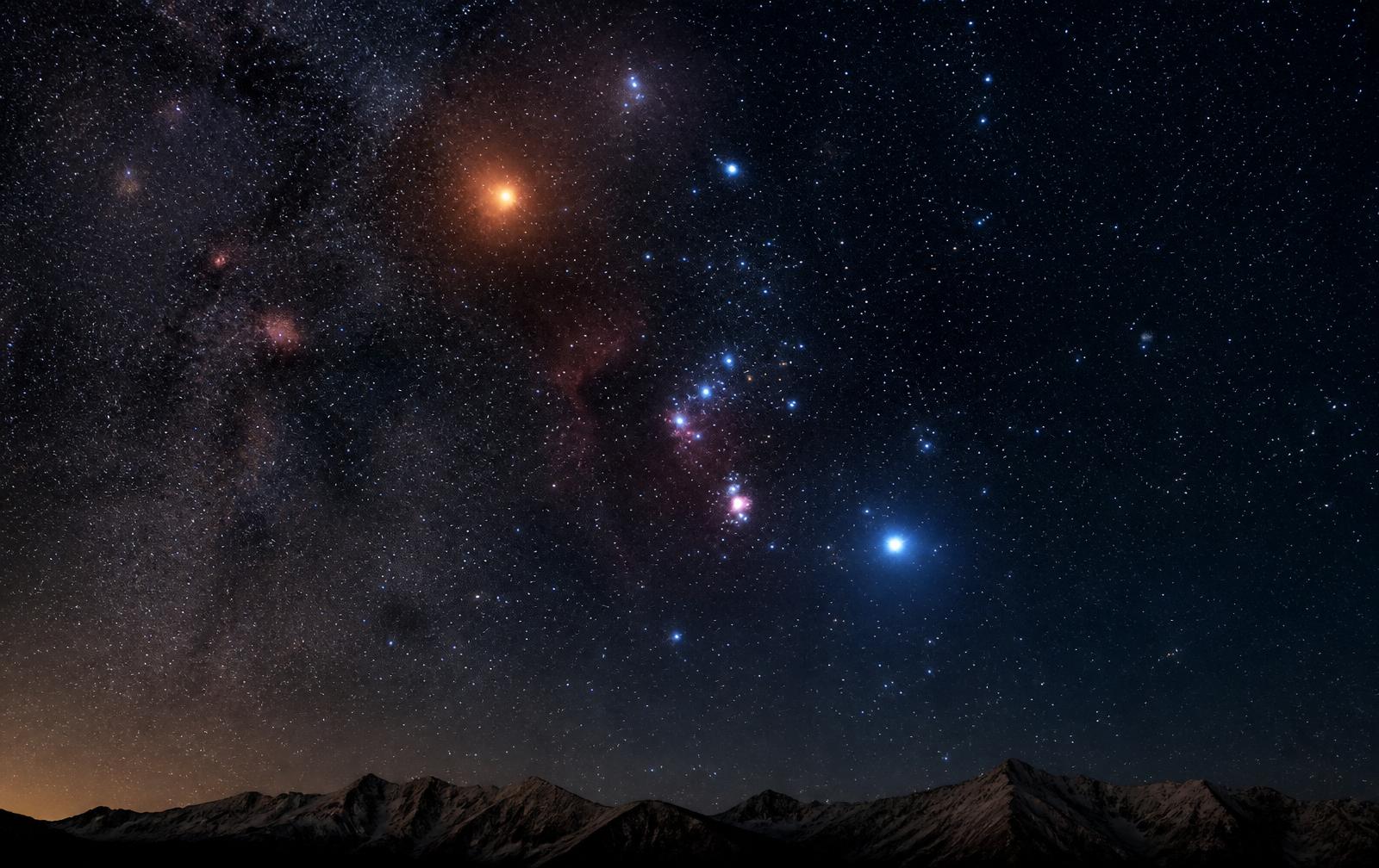 The Orion constellation rising over a mountain horizon under a deep starry sky